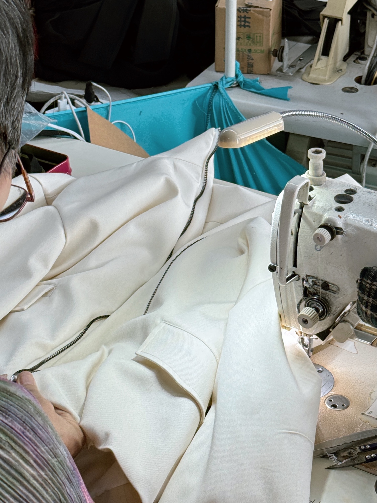 Tailor sewing an ivory garment sample at an industrial machine